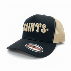 MUKA Saints black and oat trucker hat with mesh back, adjustable snap closure, and front embroidered logo.